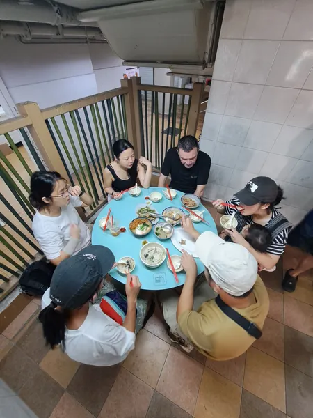 Small group sharing Cantonese-style seafood dishes at a shared table on a Singapore balcony during the hawker experience