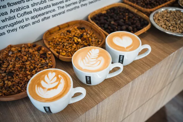 Latte art practice with three espresso cups on a wooden table, coffee beans nearby, during workshops in Singapore