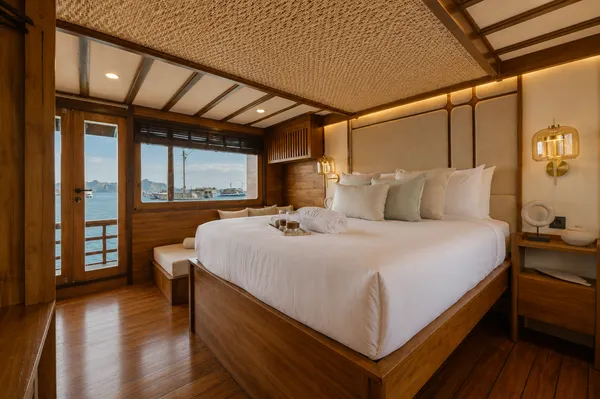 Cozy phinisi cabin bedroom on Komodo Island, with a king-size bed, warm wood finishes and sea-facing doors