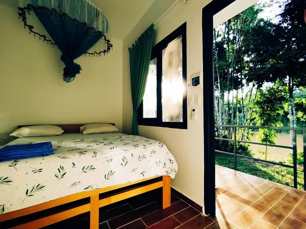Green Hope Lodge bedroom with patterned duvet and open doors to a balcony over the greenery at Cat Tien lodge stay