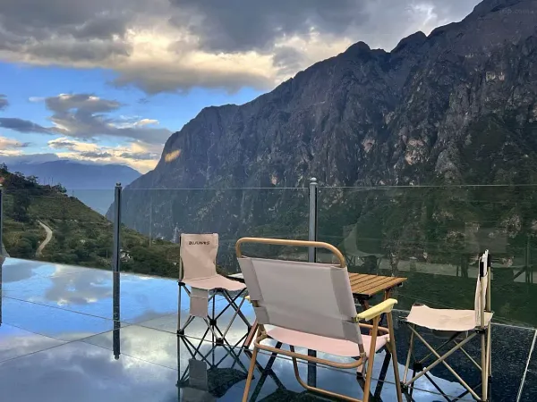 Relaxing on the glass-fronted terrace at The Bivou Lijiang, with deck chairs overlooking a river valley and steep cliffs at dusk