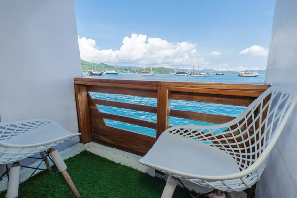 Private balcony aboard a Komodo boat with two white chairs overlooking the harbour and moored boats on a 3D2N trip in Labuan Bajo