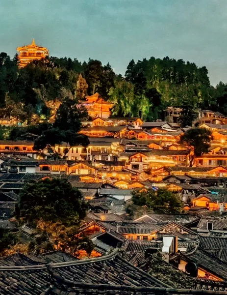 Scenic Lijiang Old Town at dusk with illuminated rooftops and a golden pagoda, ideal for Discovery More’s local food hunt