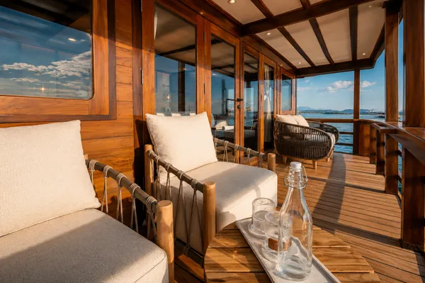 Wooden lounge deck with cushioned daybeds and a glass bottle table on a new phinisi during a Rare 3D2N trip, Komodo Island