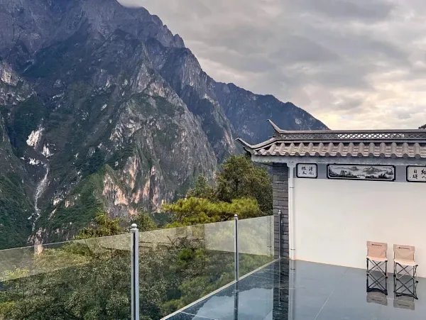 Mountain view from the glass terrace at The Bivou Lijiang in Shuhe Ancient Town, with a traditional-style roof and deck chairs