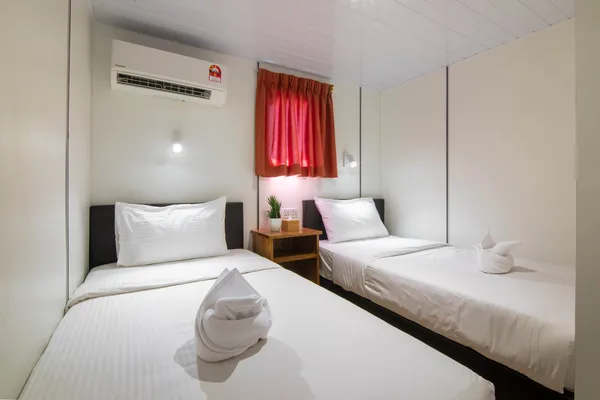 Seaventures Dive Rig cabin with two single beds, red window curtains, an air-conditioning unit and hats neatly on bedding
