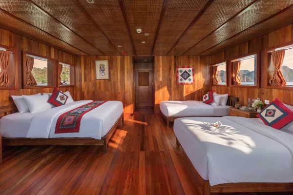 Wood-panelled cabin with two twin beds, patterned cushions and curtains, aboard a cosy boutique cruise in Cat Ba
