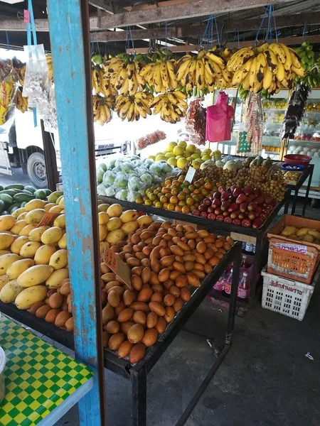 Langkawi market stall with bunches of bananas hanging above rows of tropical fruit and vegetables on wooden tables