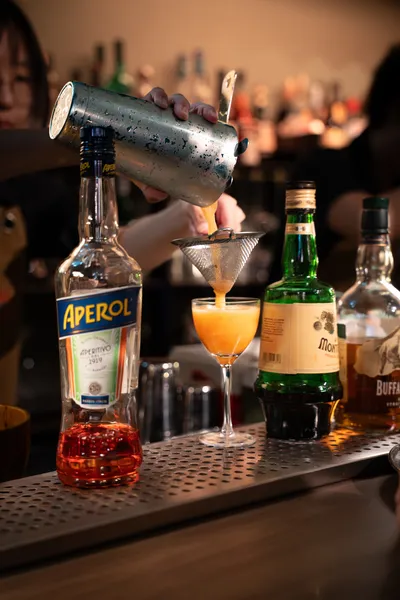 Menuangkan koktel ke dalam gelas coupe di The Magic Bar, Singapura, dengan botol Aperol dan minuman keras lain berdekatan