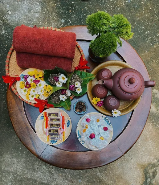 Rustic Vietnamese tea service near Hanoi: purple ceramic teapot, small cups, herbal packets and fresh flowers on a round tray