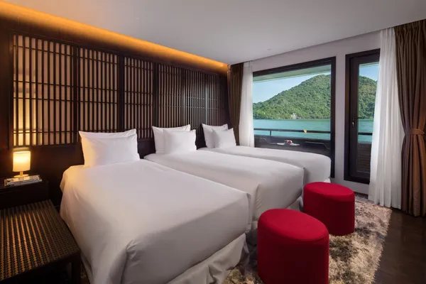 Oasis Bay Party Cruise cabin with twin beds and curtains, looking out over Halong Bay waters and limestone hills