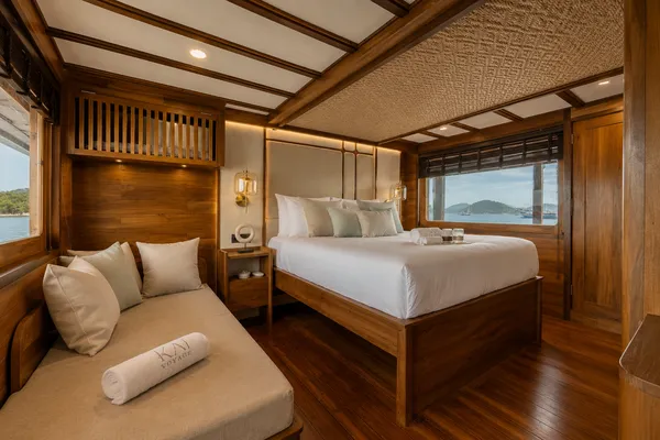 Onboard phinisi cabin with daybed and double bed, with windows framing the sea on a Komodo shared trip from Labuan Bajo
