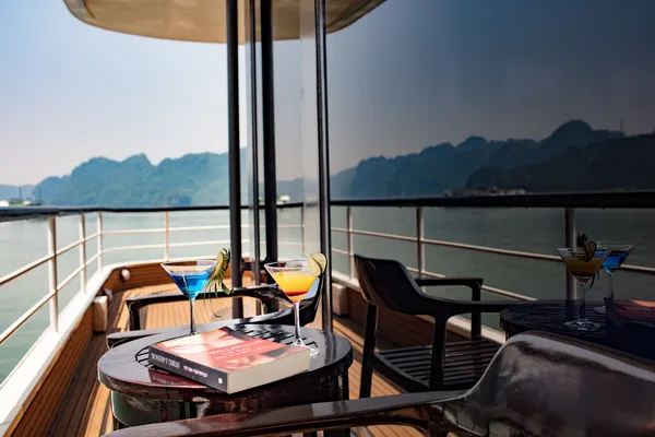 Oasis Bay Party Cruise drinks on the balcony as Halong Bay limestone karsts rise across the water today