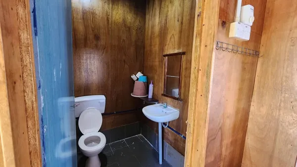 Bathroom corner with wooden walls, toilet and small sink at Luma Selakan sea lodge in Semporna, with hanging toiletries