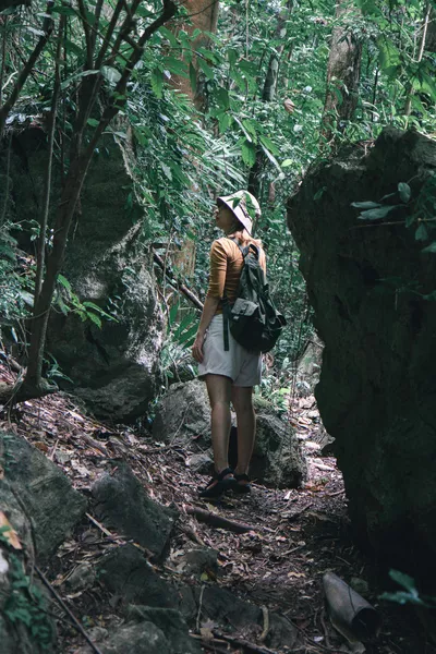 Traveller on a forest trail, holding a map, walking through thick greenery on a hike in Khao Sok National Park, Thailand