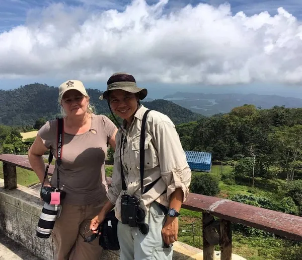 Two travellers on a hill viewpoint overlook green forest and distant hills in Langkawi during a guided nature walk