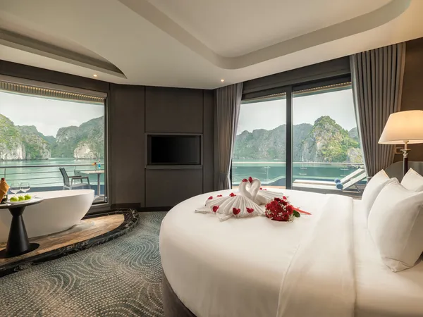 Luxurious cruise cabin with a neatly made bed and rose petals, opening onto calm bay views in Halong Bay, Vietnam