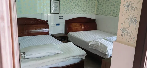Simple dorm-style room in Xishuangbanna teahouse, with three single beds, wooden headboards, and light patterned wallpaper