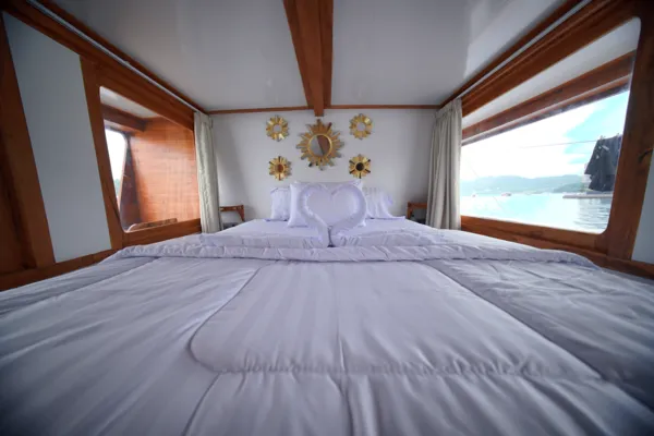 Spacious wooden boat cabin with a neatly dressed bed and wide windows facing the sea on a 3D2N Komodo trip Komodo Island