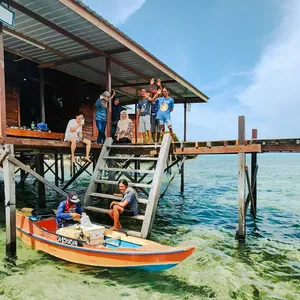 Small group boarding a skiff from a sea-lodge jetty in Semporna, wearing life jackets for a dive-and-stay day