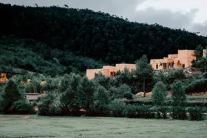 Bangunan eco-retreat Linden Centre berada di lereng bukit dalam halaman yang tenang, dikelilingi pepohonan hijau lebat dan pegunungan di kejauhan di Dali
