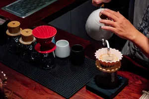 Pouring hot infusion into a dripper on a table during a rare agarwood tour in Hanoi, with small jars and tools nearby