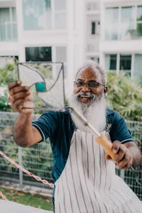 Smiling glass artist in an apron holding a patterned glass panel outdoors in Singapore, centrepiece craft—workshops in Singapore