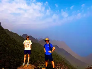 Two hikers pose on a ridge with layered mountain silhouettes behind them on Mt Fansipan in Sapa during a 1-day eco trek