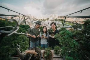 Three people smiling while holding bonsai pots on a terrace during a Japanese-style tropical bonsai workshop in Singapore