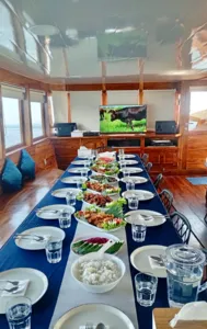 Set dining table aboard a wooden phinisi with shared plates, bowls and drinks during a 3D2N cruise to Komodo Island