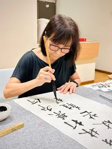 Singapore Chinese calligraphy lesson with a woman writing black characters in ink strokes on rice paper with a brush