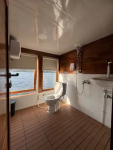 La Famille boat bathroom with toilet, shower fittings and open-water view through the window on a Komodo cruise Labuan Bajo