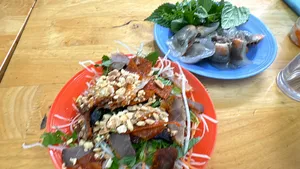Assorted Hanoi street-food—grilled meats with herbs—served on a red plate on a wooden table for a Zero‑Tourist food adventure