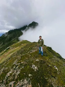Hiker standing on a misty alpine ridge above the clouds, surrounded by green slopes, on a guided hike to Jade Dragon Snow Mountain in Lijiang