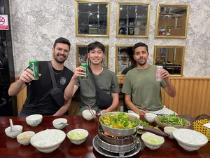 Travellers seated at a restaurant table with a shared hot pot and small bowls, enjoying a small-group Hanoi food adventure