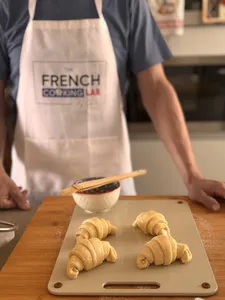 Di bengkel di Singapura, pembuat pastri dari French Cooking Lab menyusun doh croissant di atas papan kayu, dengan dulang dan peralatan berdekatan