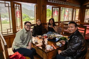 Group sharing a meal inside a traditional dining room in Shangri-La, with large windows framing a green mountain valley