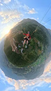Paraglider passenger glides above green valley ridges at sunset, suspended under the paraglider canopy in Sapa