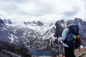 Backpacker with trekking poles overlooks a snowy valley and turquoise water in Shangri-La, hiking at high altitude