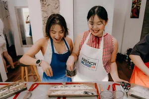 Participants in aprons preparing French baguettes, sprinkling herbs on dough with a jar at French Cooking Lab workshops in Singapore