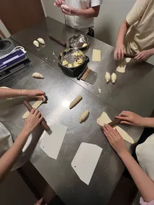 Hands shaping small dough pieces and rolls around a shared workspace at a shio pan baking workshop during workshops in Singapore