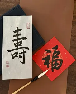 Chinese calligraphy sheet with bold black characters, a brush and red envelope on a wooden table for calligraphy workshops in Singapore