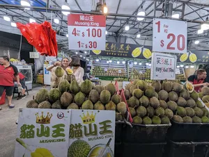 Durian stall in a Singapore market hall with piles of Musang King fruit and price signs, on a Geylang night walk
