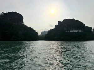 Sunlit waters in Kilim Geoforest Park, Langkawi, with jungle-clad cliffs and a shimmering wake from a cruise boat