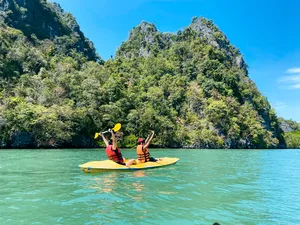 Two people kayaking across clear green water beside forested limestone cliffs in Langkawi during a Kilim Geoforest nature tour