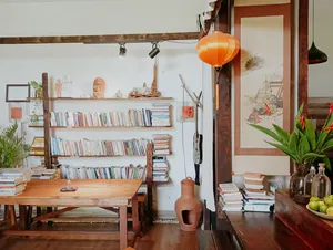 Sudut tenang di Chan Dat Living Room di Hoi An, dengan rak buku kayu, meja belajar, dan lentera oranye yang bercahaya