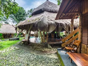 Thatched-roof veranda with wooden chairs, pebbled paths and a lush garden at Omunity Bali retreat in Bali