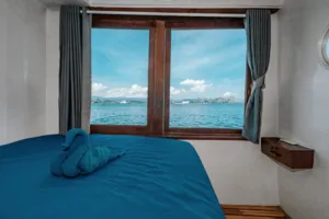 Private 3D2N Komodo cruise cabin with a neatly turned bed by the window, sea and hills visible outside, Labuan Bajo
