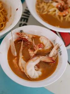Bowls of prawn noodle soup in orange broth with fresh shrimp, served at an eatery on a Joo Chiat food tour