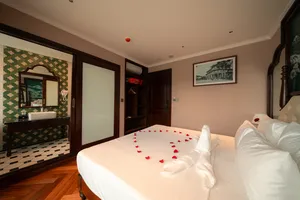 Cruise cabin bedroom with mirror and bathroom doorway, king bed with rose‑petal towel swans, Cat Ba 2D1N